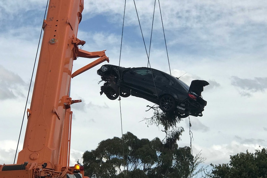 A car being lifted into the air by a crane.