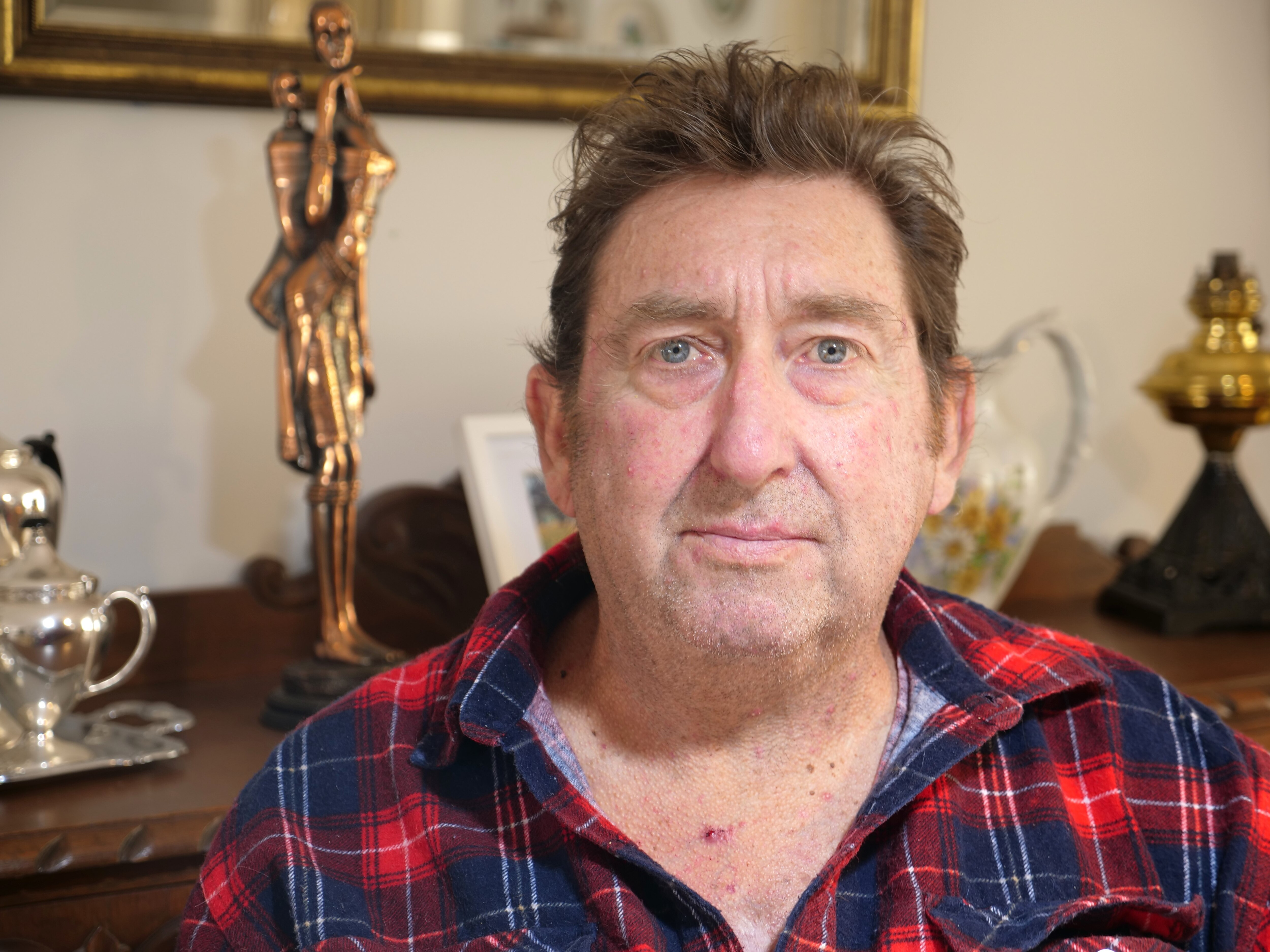 A close up photo of a seated man with a number of old house items behind him
