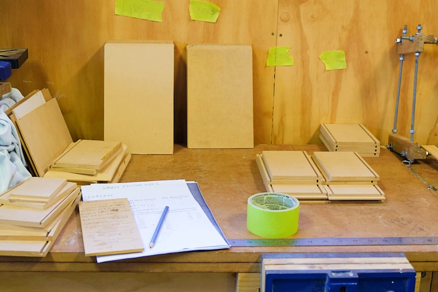 A work bench with pre-cut pieces of wood ready to be assembled into a small coffin.