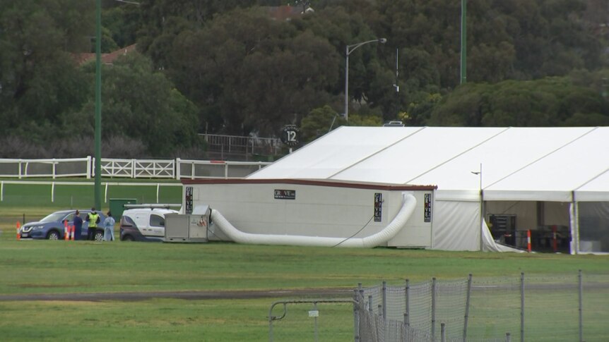 A very large white tent with a ventilation tube and several workers wearing PPE in the far distance.