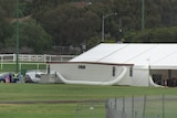 A very large white tent with a ventilation tube and several workers wearing PPE in the far distance.