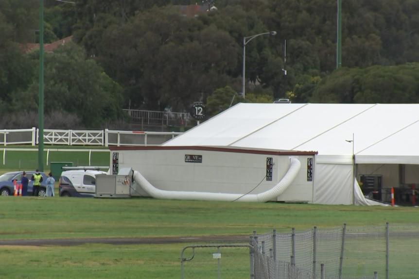 A very large white tent with a ventilation tube and several workers wearing PPE in the far distance.