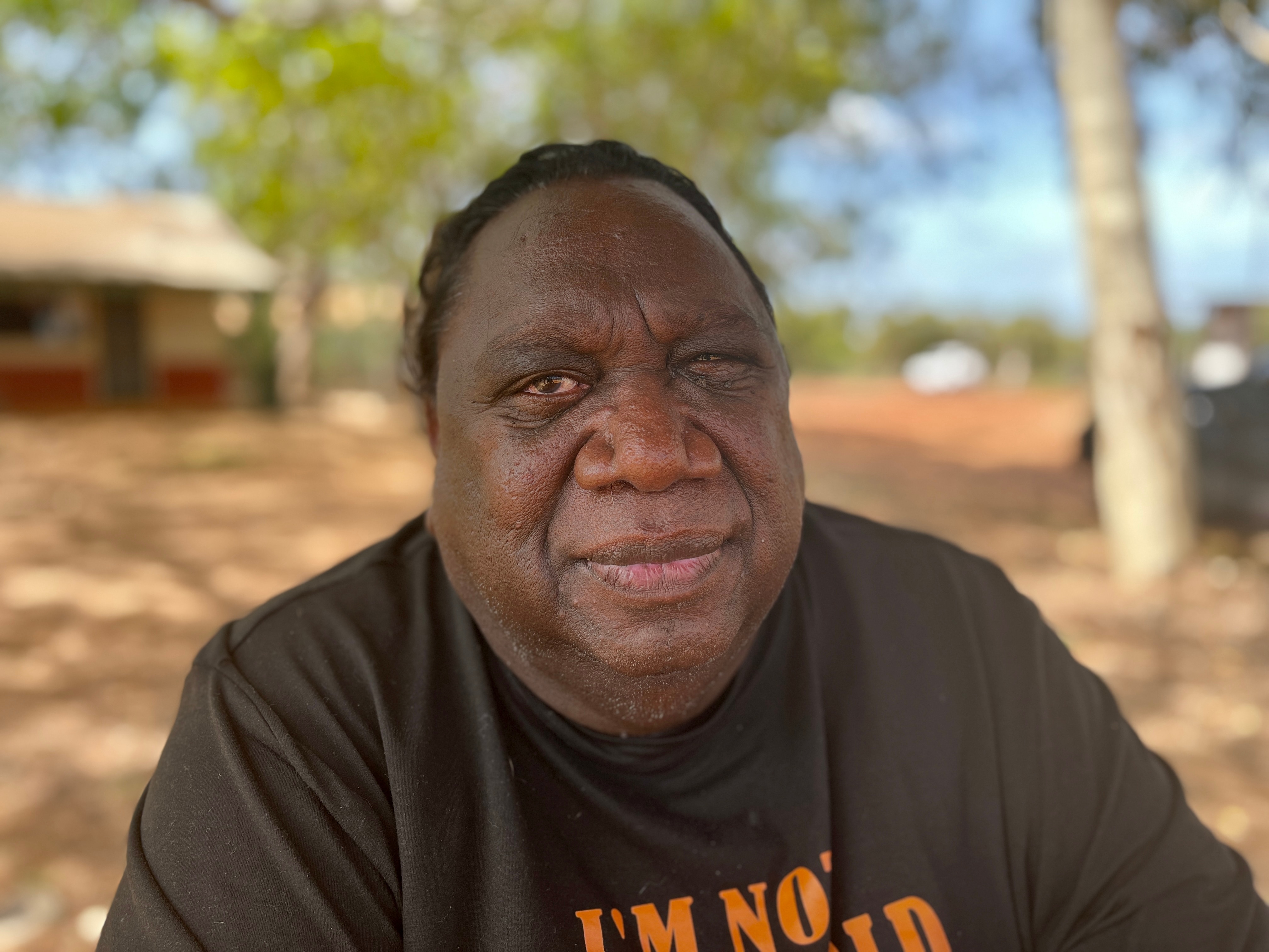 Aboriginal man wearing a black top sitting outside.