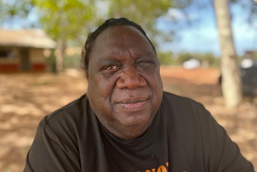 Aboriginal man wearing a black top sitting outside.