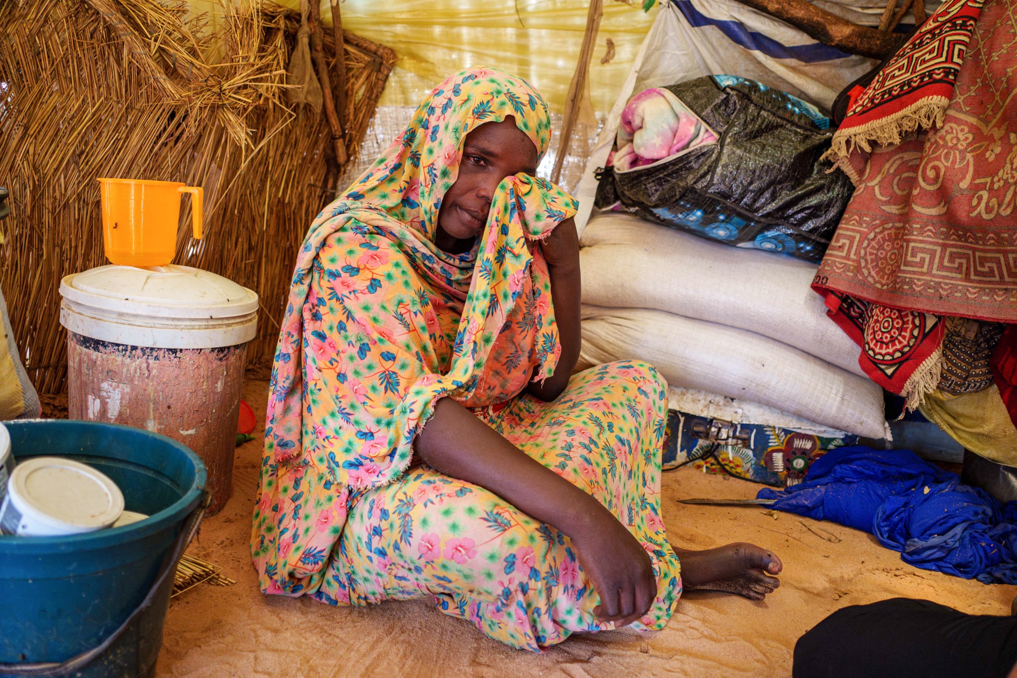 A woman wearing a colourful dress and hijab wipes tears from her eyes.