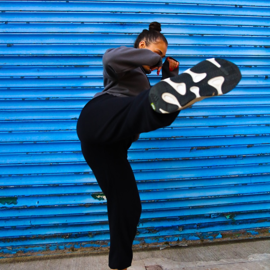 A woman wearing black kicks high into the air against a blue roller door