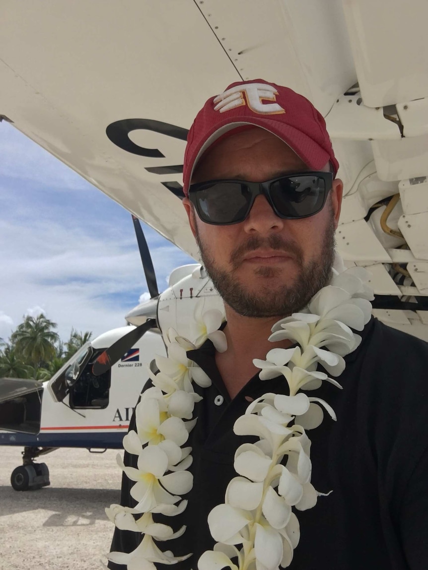 Head shot of Mark Willacy with floral leis around his neck standing in front of aeroplane.