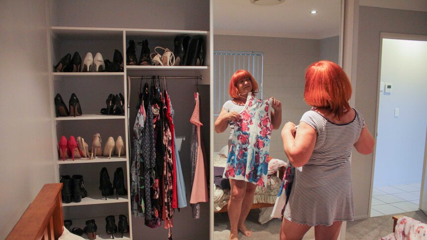 Emily Wells holding up a dress, while looking in her bedroom mirror.