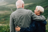 An older couple hug as they admire a beach view