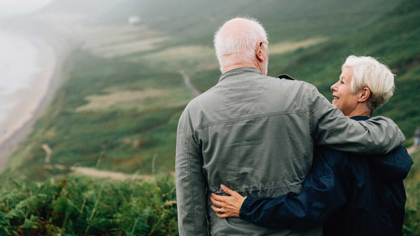 An older couple hug as they admire a beach view