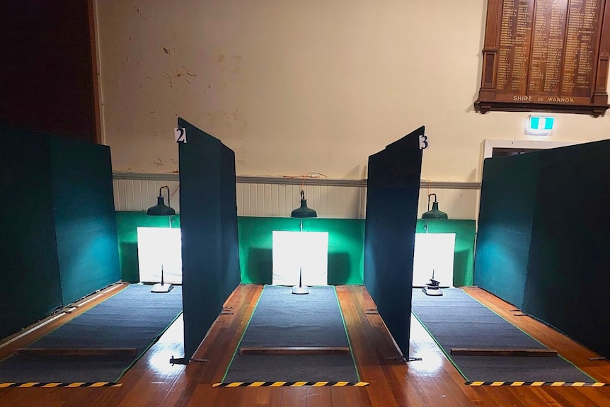 A dimly lit hall setup with black cloth partitions and long length of carpet and quoits pegs