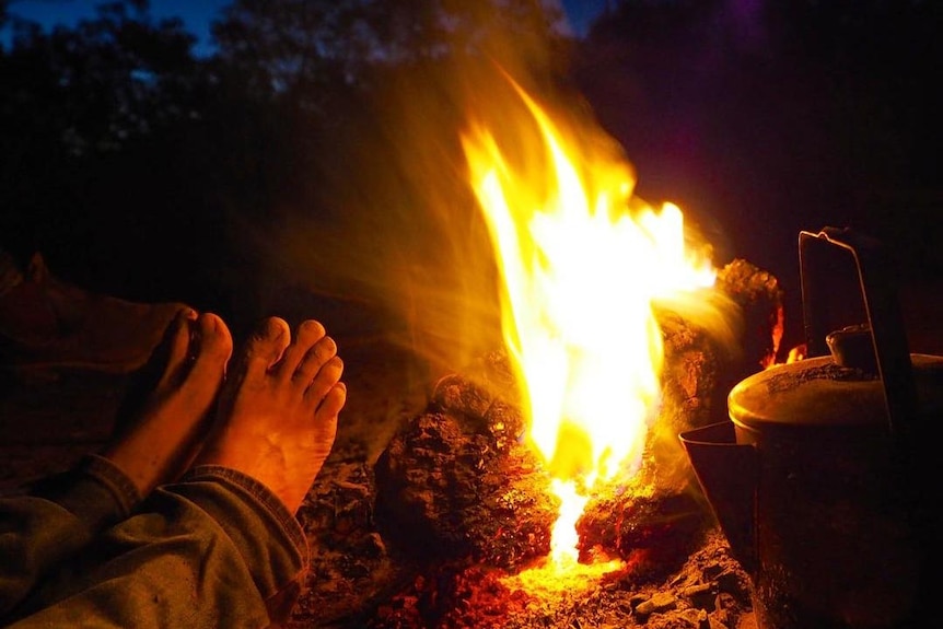 View of photographer's feet warming against a campsite fire at night.