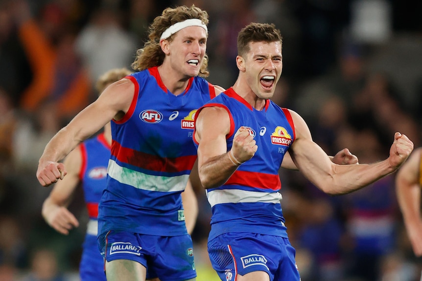 Josh Dunkley smiles and clenches both fists as Aaron Naughton hugs him from behin