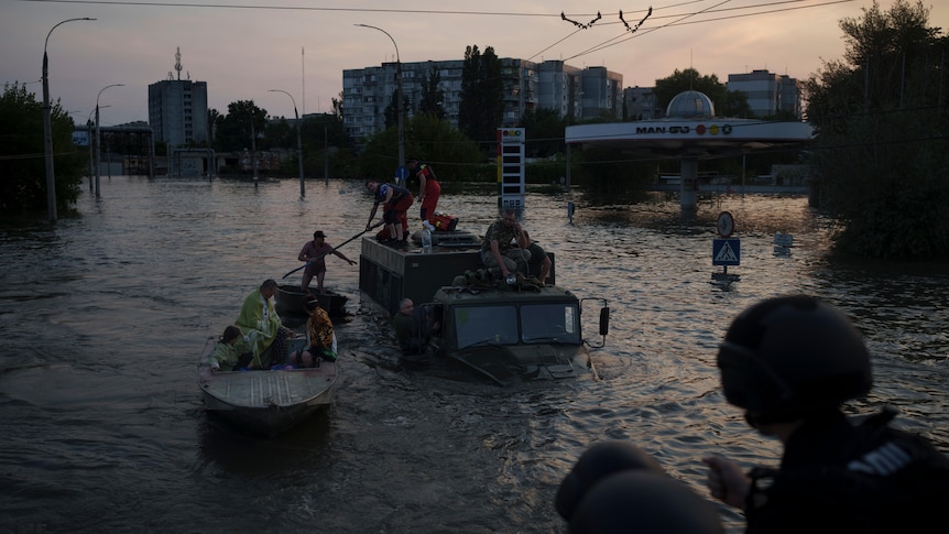 In very low light, people are rescued from the top of a military truck and into a small boat. 