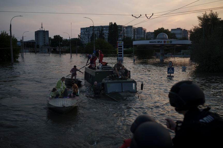 In very low light, people are rescued from the top of a military truck and into a small boat. 