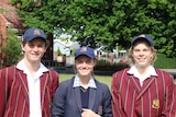 Three smiling high school students wearing caps standing outside