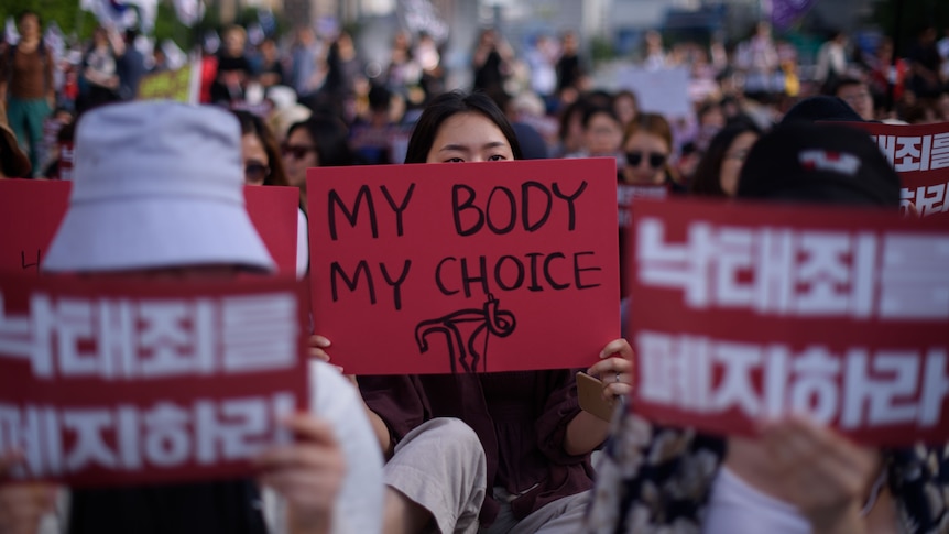 A South Korean protester holding sign saying 'my body my choice' among a sea of protesters.