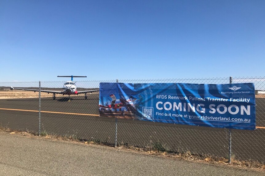 A banner that says "Coming soon" in front of a plane at an airport.