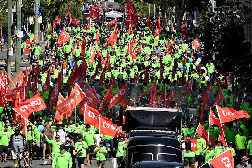 Hundreds of people in bright green shirts waving red banners in a parade.