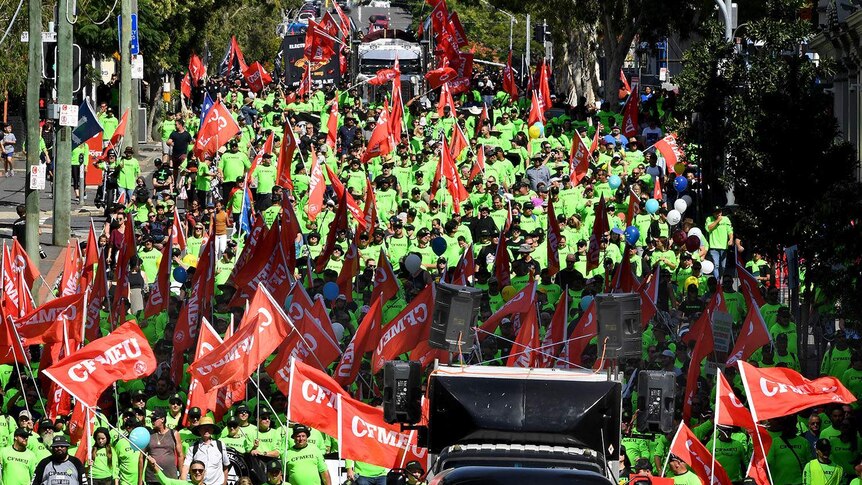 Hundreds of people in bright green shirts waving red banners in a parade.