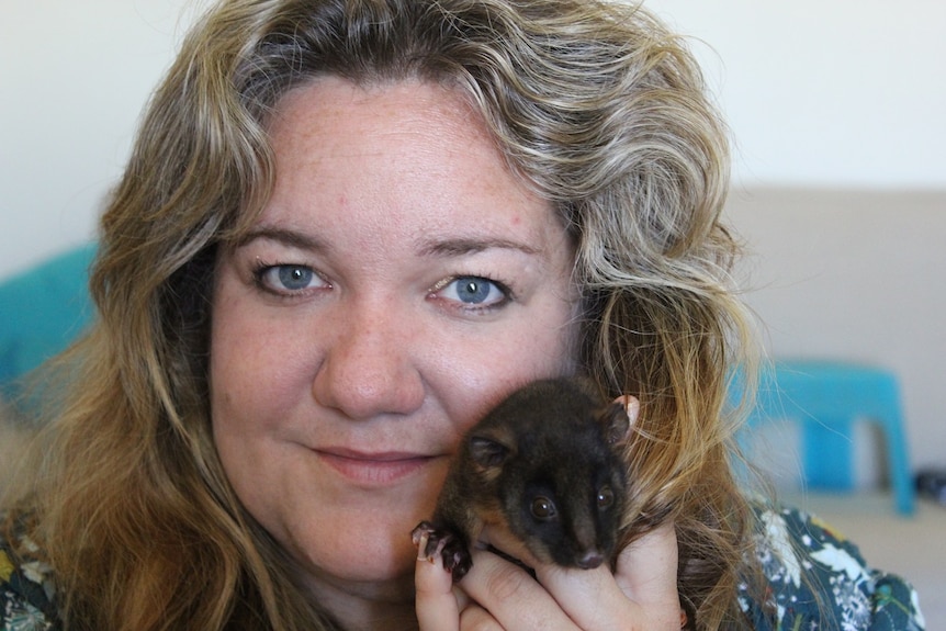 A woman holds a tiny possum.