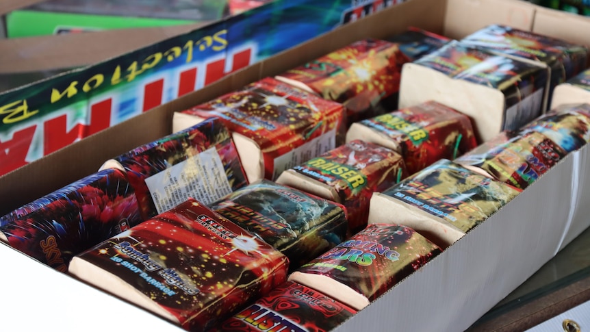 Several retail fireworks placed in front of a cardboard box. 