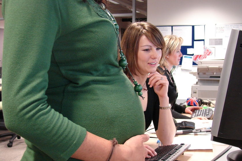 Pregnant woman holding belly at work.