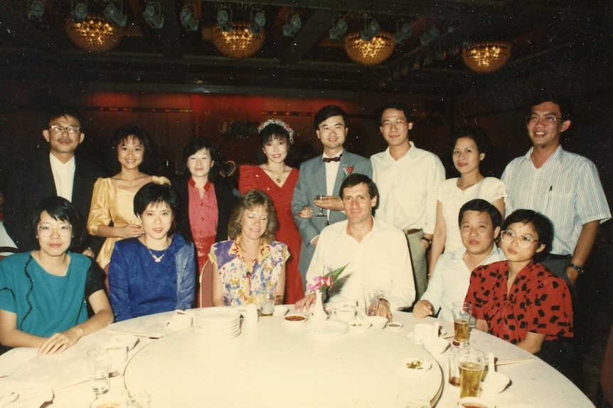 A vintage photo with a group of people sitting at a lazy susan looking at the camera