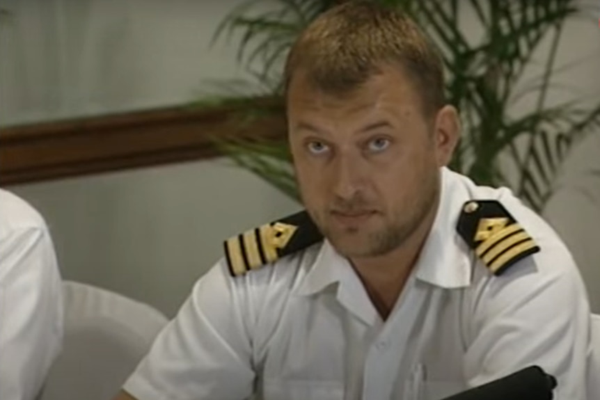 Freeze-framed image of Christian Maltau, with short hair, in white sailing uniform shirt, looks ahead with serious expression.