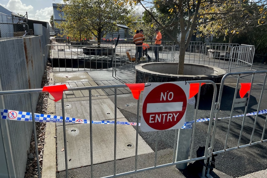 Three men wearing orange work clothes look at a hole behind a no entry sign