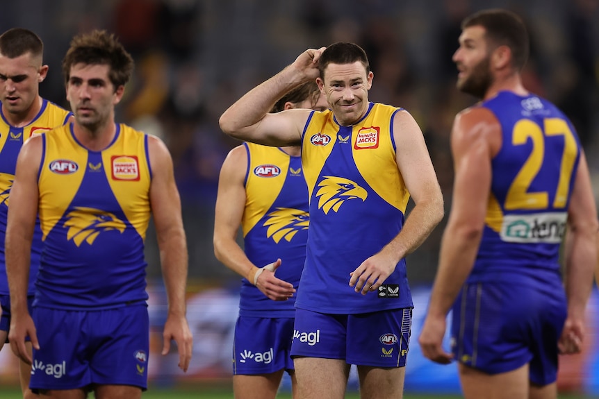 Jeremy McGovern grimaces and puts his hand on his head while standing around teammates