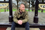 Marcus Pattie sits on a step of a rotunda in a park.