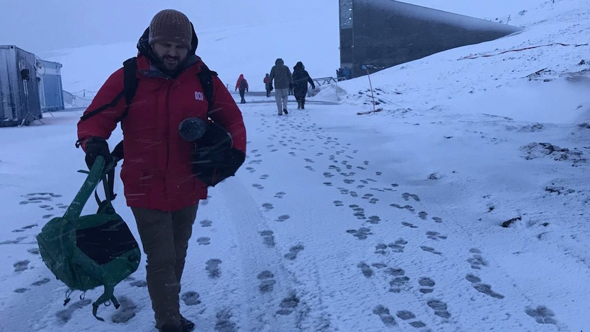 Steven Schubert walking through sleet with camera in Svalbard Norway while covering Doomsday Vault story.