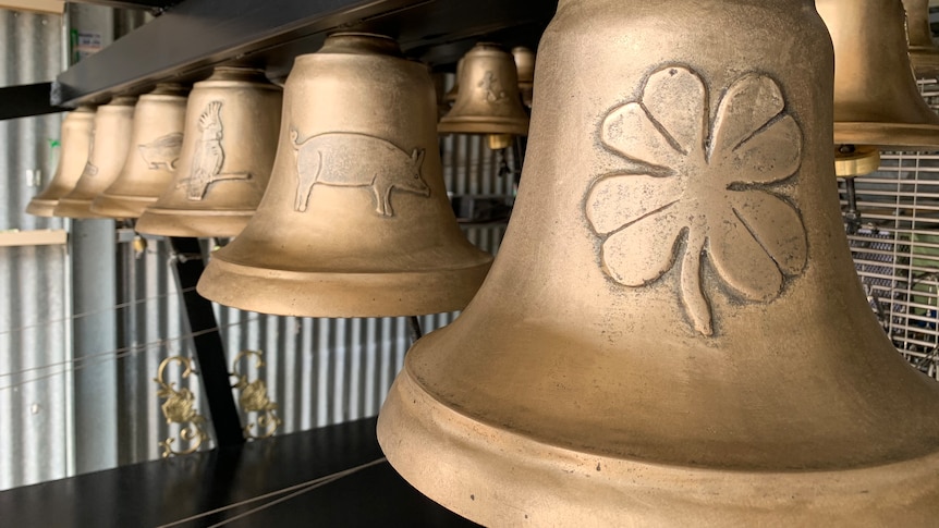 A line of gold bells with designs including four leaf clover, pig and cockatoo on them