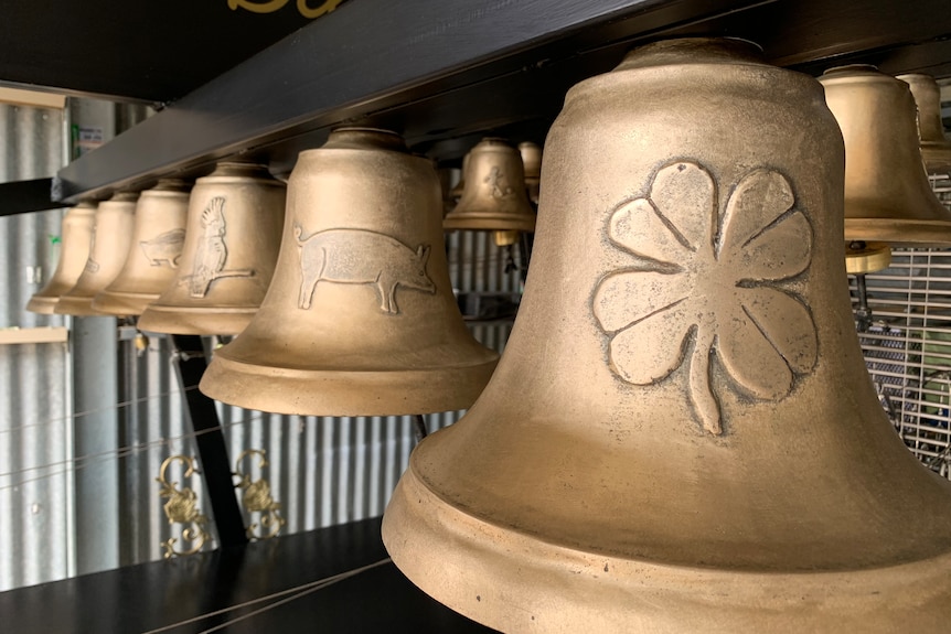 a line of gold bells with designs including four leaf clover, pig and cockatoo on them