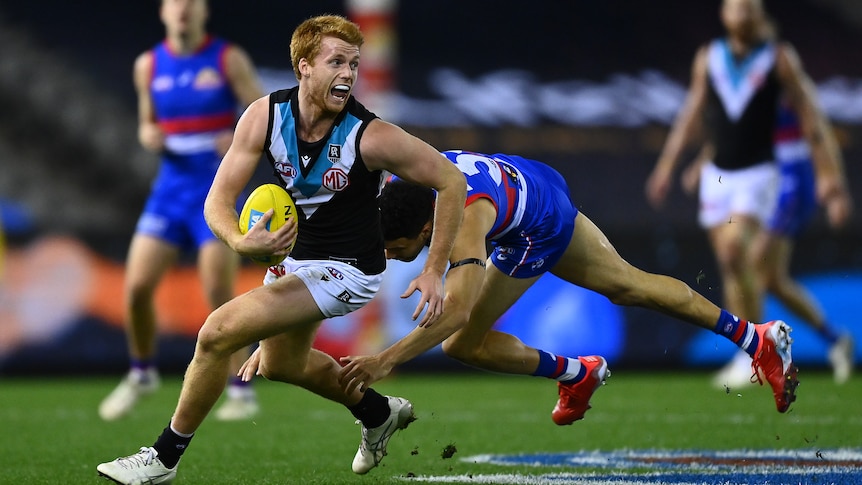 A Port Adelaide midfielder looks upfield as he cuts back to evade a diving tackle from a Western Bulldogs player.
