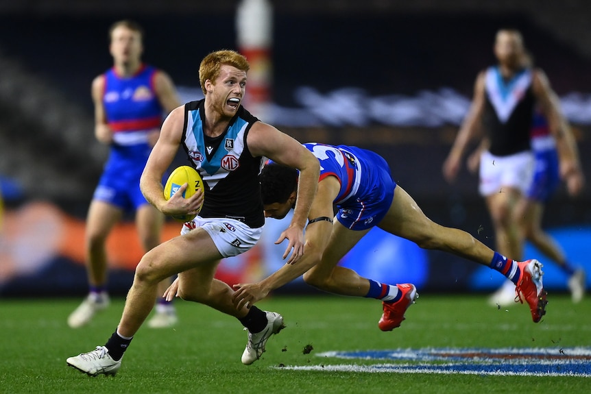 A Port Adelaide midfielder looks upfield as he cuts back to evade a diving tackle from a Western Bulldogs player.