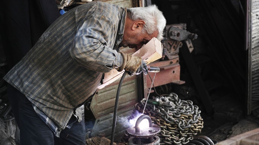 A man with grey hair bends over metal work in a workshop