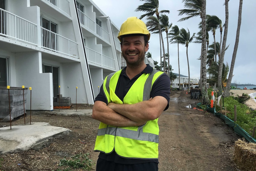 A man in a hard hat stands in front of a block of units