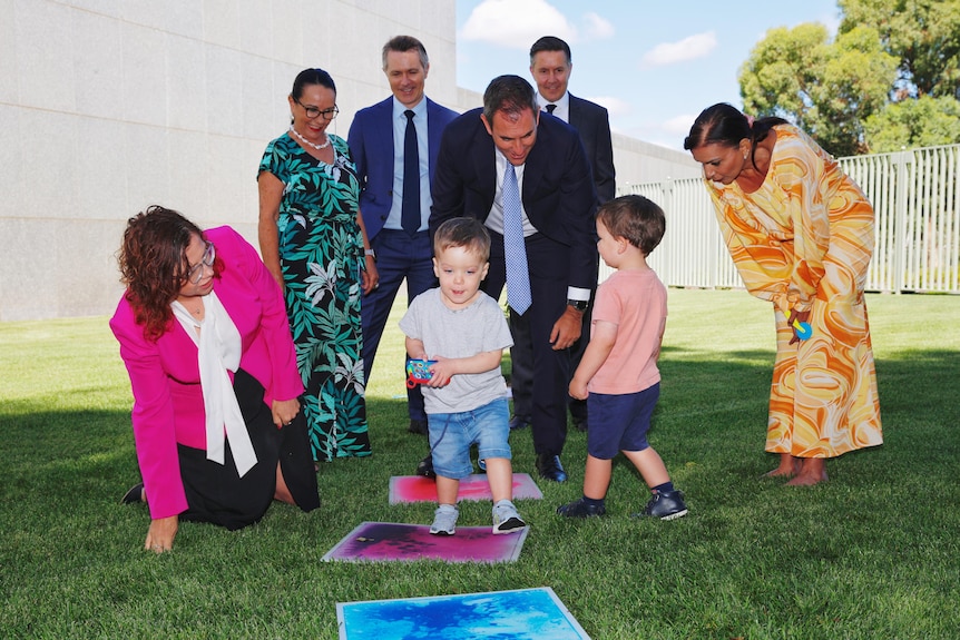 Amanda Rishworth, Linda Burney, Jason Clare, Jim Chalmers, Mark Butler and Anne Aly standing on a lawn with two young children.