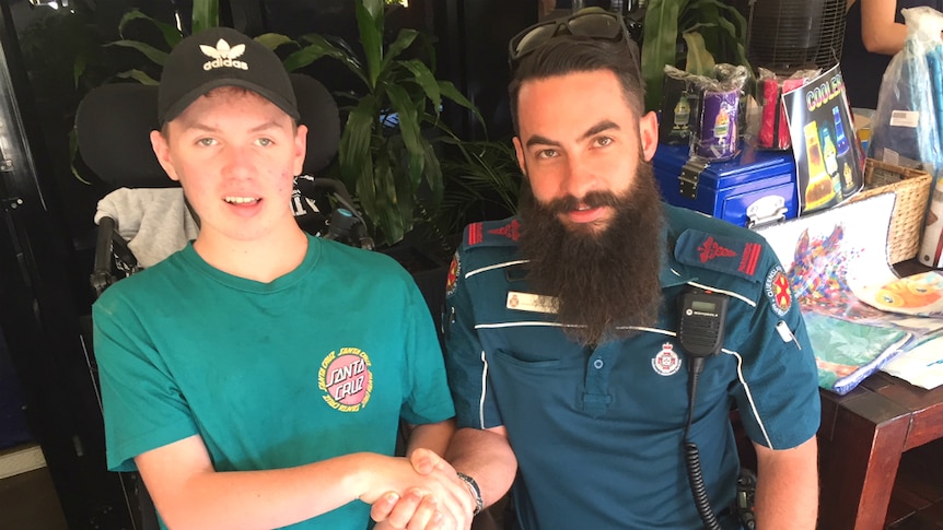 Teenage boy in a wheelchair holds the hand of a paramedic who saved his life