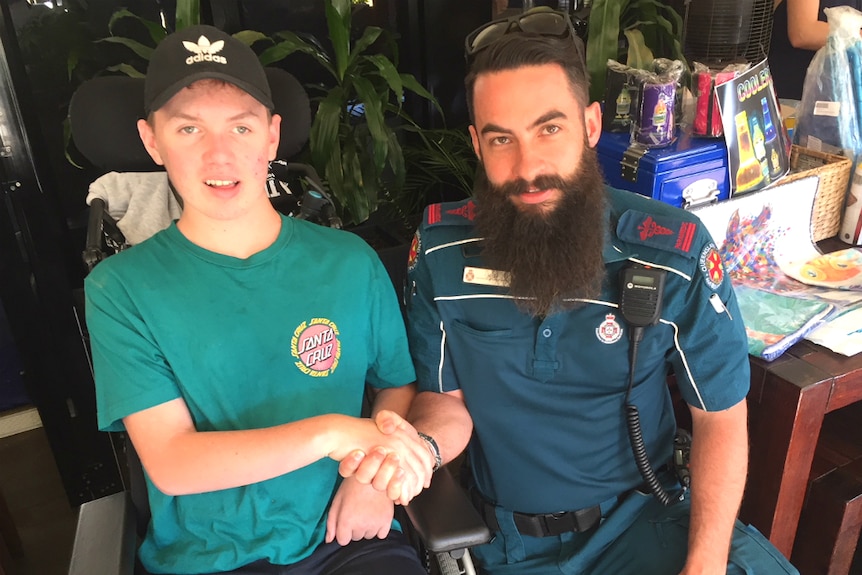 Teenage boy in a wheelchair holds the hand of a paramedic who saved his life