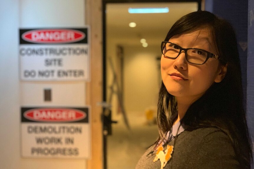 Jenny Zhang stands in front of a doorway with 'construction site do not enter' signs next to it.