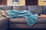 A woman lies on a couch covered in a blanket.
