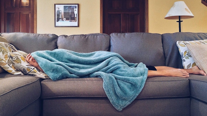 A woman lies on a couch covered in a blanket.