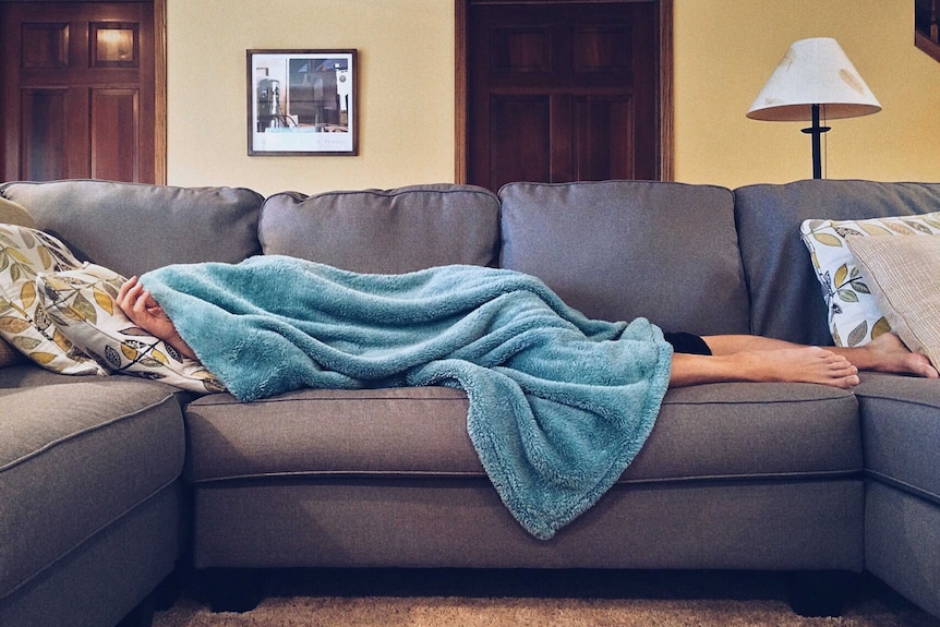 Person lying on couch under a blanket