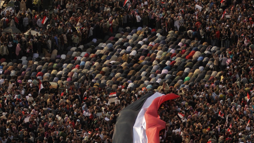 Anti-government demonstrators hold a huge Egyptian flag as others pray at Cairo's Tahrir Square.