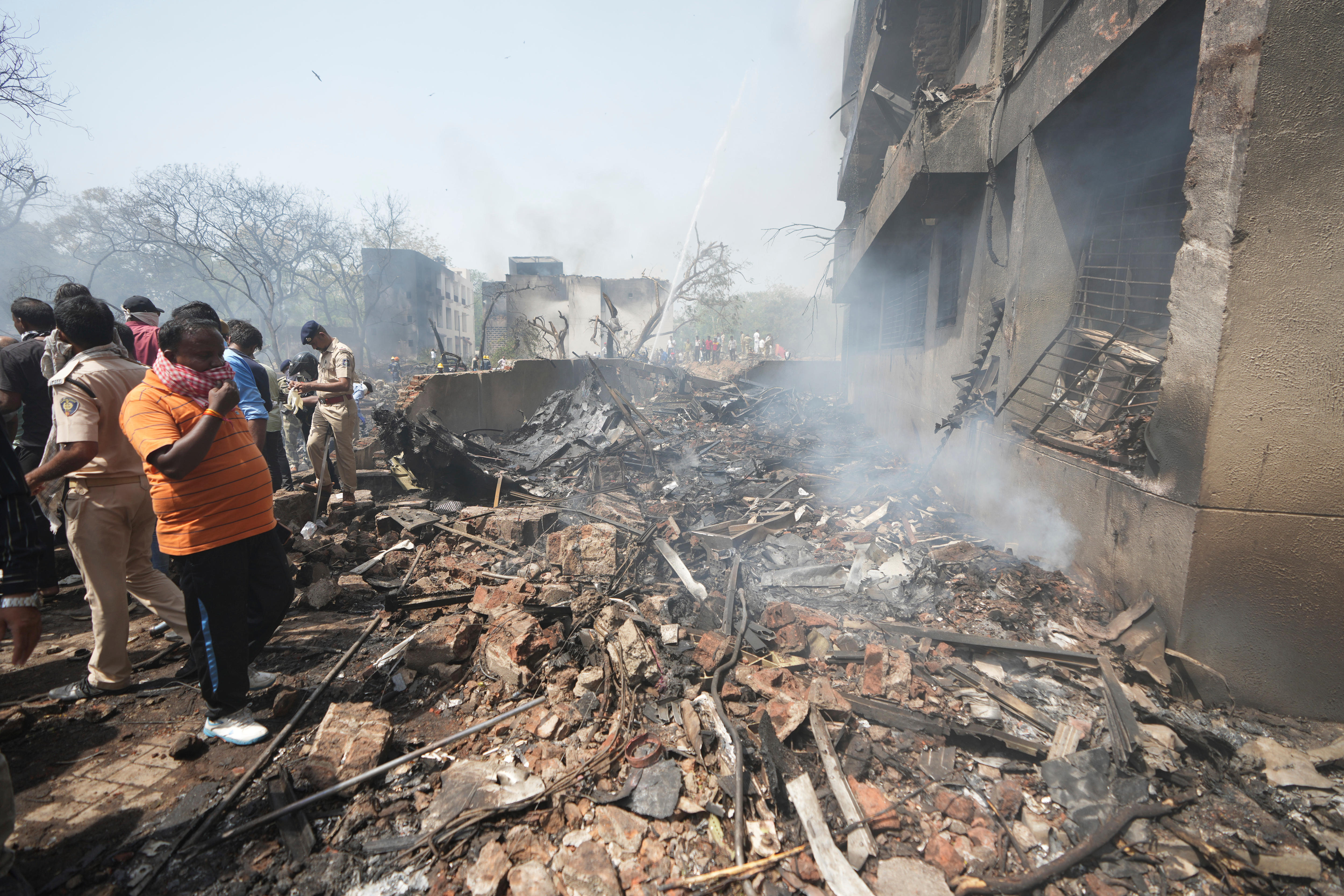Men and police officers standing alongside a pile of bricks and debris and a charred and crumbling building