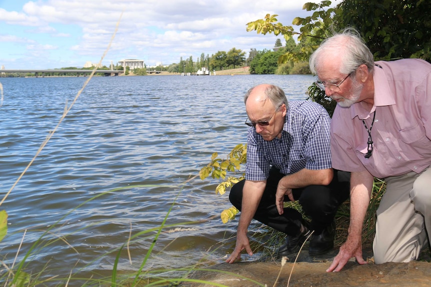 Mark Butz and Dr Doug Finlayson inspect a limestone rock beside Lake Burley Griffin.