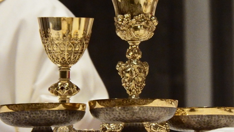 Two gold chalices and three bowls containing communion wafers.